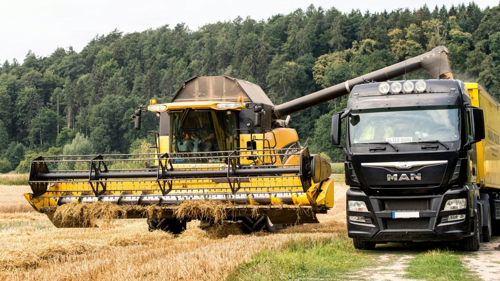 Yellow harvester working alongside a MAN truck in a European rural field.